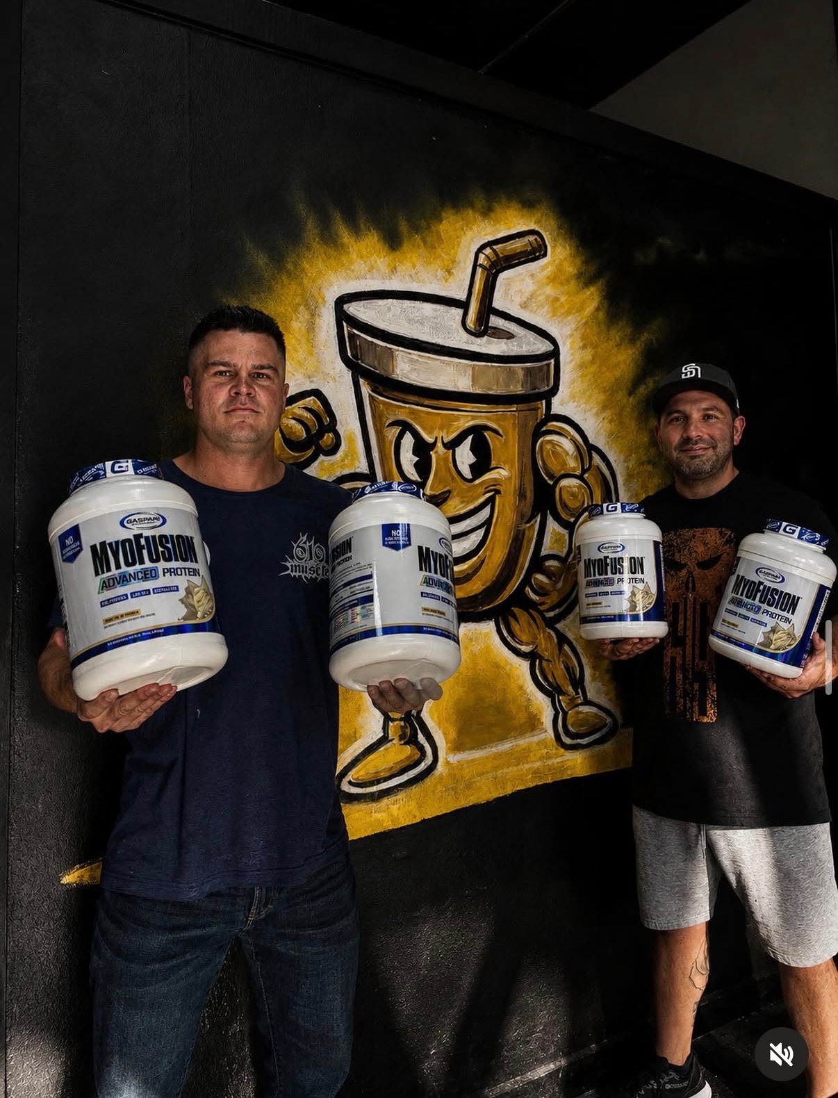 The Muscle Lounge founders in front of the mascot mural